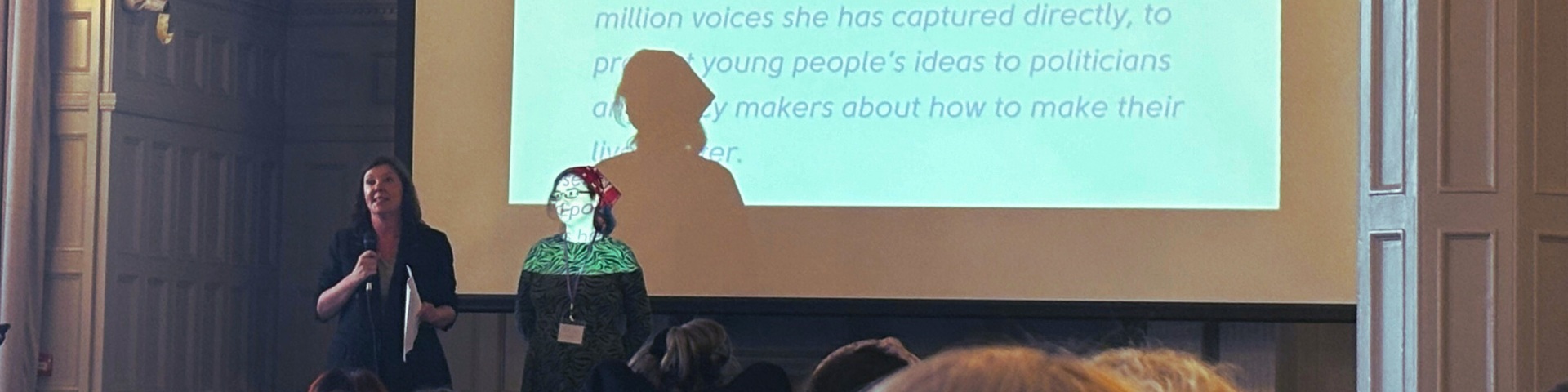 Photograph of Dame Rachel de Souza and Rae Sloan in front of a presentation screen