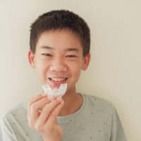 Photograph of teen smiling, holding a mouthguard