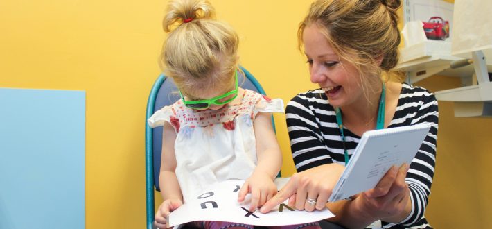 Child reading eye test book sat next to adult