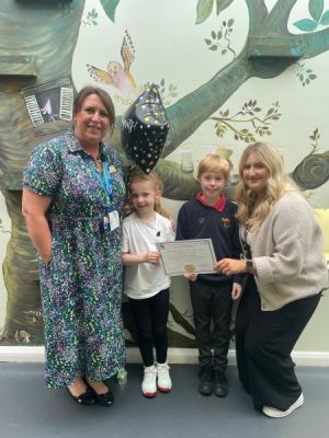 Photo of Ballifield Primary School, Sheffield, being presented with Asthma Friendly Schools Certificate. 2 adults, 2 children featured in front of a mural